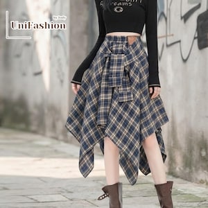 May include: A long, asymmetrical plaid skirt featuring a blue, tan, and white checkered pattern with a decorative fabric tie at the waist. The skirt is paired with a black long-sleeved top. The text UniFashion by Jody is visible in the upper left corner.