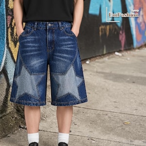 May include: Blue denim shorts featuring large star designs on the front. The shorts have a classic five-pocket design and a button and zipper closure. The shorts are worn with a black t-shirt and white socks.