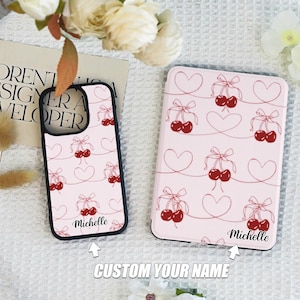 May include: Two phone cases with a pink background and a pattern of red cherries with pink bows and hearts. The text "Michelle" is on both cases.