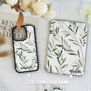 May include: Two phone cases with a white background and a green olive branch pattern. The cases have black borders and the name "Michelle" is printed on each case.