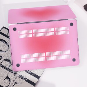 May include: A pink laptop case with a gradient design, shifting from a darker red shade in the middle to a lighter pink at the borders. It has ventilation slots and black rubber feet.