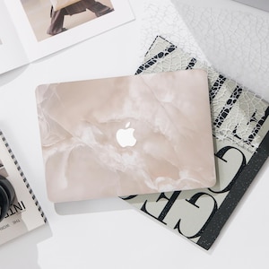 May include: A laptop computer with a pink and white marble design skin. The Apple logo is visible on the lid.