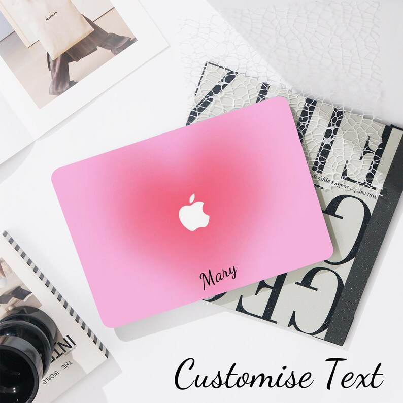 May include: Pink laptop case with a gradient effect and a white Apple logo. The name "Mary" is printed in black script. The words "Customise Text" are written in a script font at the bottom of the image.