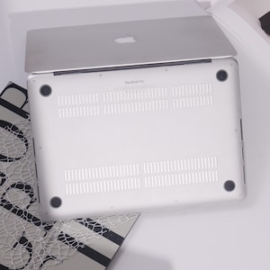 May include: Silver MacBook Pro laptop with the Apple logo on the lid. The underside is white with ventilation slots and four black rubber feet. The words "MacBook Pro" are printed on the bottom of the laptop.