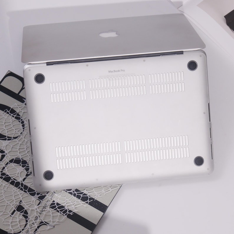 May include: Silver MacBook Pro laptop with the Apple logo on the lid. The underside is white with ventilation slots and four black rubber feet. The words "MacBook Pro" are printed on the bottom of the laptop.