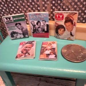 Puede incluir: Cinco revistas en miniatura de TV Guide vintage sobre una mesa turquesa con una moneda de veinticinco centavos de d&oacute;lar de plata. Las revistas presentan portadas con fotos de Dick Van Dyke,  "TV Guide" y "TV News".