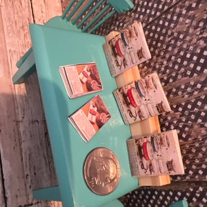 Puede incluir: Una mesa de color turquesa con tres anuncios de revistas vintage sobre ella. La mesa est&aacute; hecha de madera y tiene un acabado turquesa claro. Las revistas son todas sobre electrodom&eacute;sticos de cocina y tienen un dise&ntilde;o retro. Hay una moneda de plata sobre la mesa.