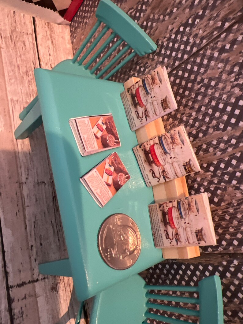 Puede incluir: Una mesa de color turquesa con tres anuncios de revistas vintage sobre ella. La mesa est&aacute; hecha de madera y tiene un acabado turquesa claro. Las revistas son todas sobre electrodom&eacute;sticos de cocina y tienen un dise&ntilde;o retro. Hay una moneda de plata sobre la mesa.