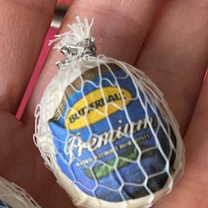 May include: A small, white, round object wrapped in a clear plastic mesh bag. The bag has a blue and yellow label that reads "Butterball Premium".