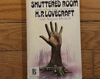 Puede incluir: Un libro de bolsillo titulado "The Shutter Room" de H.P. Lovecraft y August Derleth. La portada presenta una mano que emerge de un tronco de árbol en un entorno de bosque. El libro forma parte de la edición Arkham de H.P. Lovecraft.