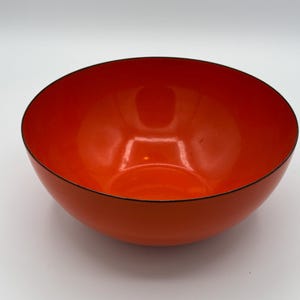 May include: A vibrant orange bowl with a glossy finish and a thin black rim. The bowl's interior reflects light, highlighting its smooth surface. This kitchenware item is suitable for serving food or as a decorative piece.