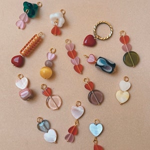 May include: Assortment of colorful heart-shaped charms with gold accents. The charms feature various materials, including glass, wood, and metal. Some charms are strung together with multiple hearts, while others are single hearts. The charms are perfect for adding a touch of whimsy to jewelry or other crafts.
