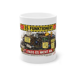 Könnte beinhalten: Weißer Keramikbecher mit detailliertem Grafikdesign. Das Design zeigt eine komplexe Maschine mit verschiedenen Komponenten, Text auf Deutsch und eine Quietscheente. Der Becher hat ein gelb-schwarzes Warnbanner mit der Aufschrift "ES FUNKTIONIERT" und "FASS ES NICHT AN."