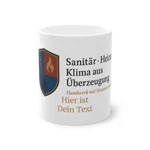 Peut inclure: Mug en céramique blanche avec un motif imprimé. Le motif comprend un écusson avec une flamme et des outils, ainsi qu'un texte en allemand. Le texte sur le mug dit "Sanitär-Heiz Klima aus Überzeugung" et "Hier ist Dein Text".