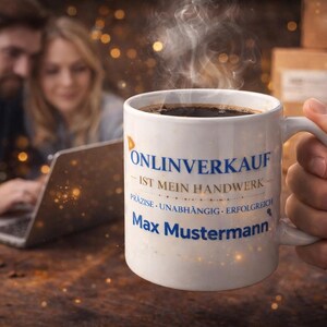 Op de afbeelding: Een witte koffiemok gevuld met donkere koffie, vastgehouden door een hand. De mok heeft Duitse tekst: "Onlineverkauf ist mein Handwerk" en de naam "Max Mustermann". Stoom stijgt op van de koffie. Een stel is wazig op de achtergrond.