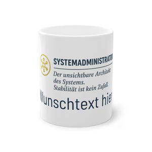 Könnte beinhalten: Weißer Keramikbecher mit dem Text "SYSTEMADMINISTRATOR" und deutschem Text. Der Becher hat eine goldfarbene Grafik und zusätzlichen Text in dunkelblauer Schrift. Der Becher ist zylindrisch und scheint leer zu sein.