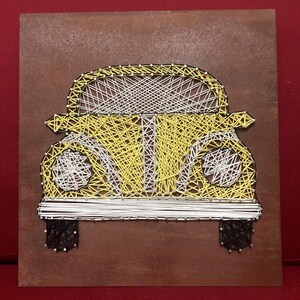 Può includere: Un'opera d'arte con fili raffigurante un'auto gialla su un quadrato di legno marrone. La carrozzeria dell'auto è realizzata con filo giallo, mentre il filo bianco forma i finestrini e i dettagli. Il filo nero crea le ruote.