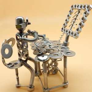 May include: A silver metal sculpture of a person playing a drum kit. The sculpture is made of nuts, bolts, and washers. The person is sitting on a stool and has a microphone in front of them. There is a music stand behind the person.