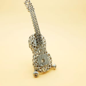 May include: A silver metal guitar sculpture made from nuts and bolts. The guitar is on a small stand and is angled slightly to the right.