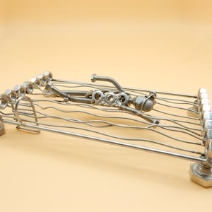Puede incluir: Una escultura de metal de un nadador hecha de tuercas, tornillos y alambre. La escultura está tumbada sobre un marco de alambre.