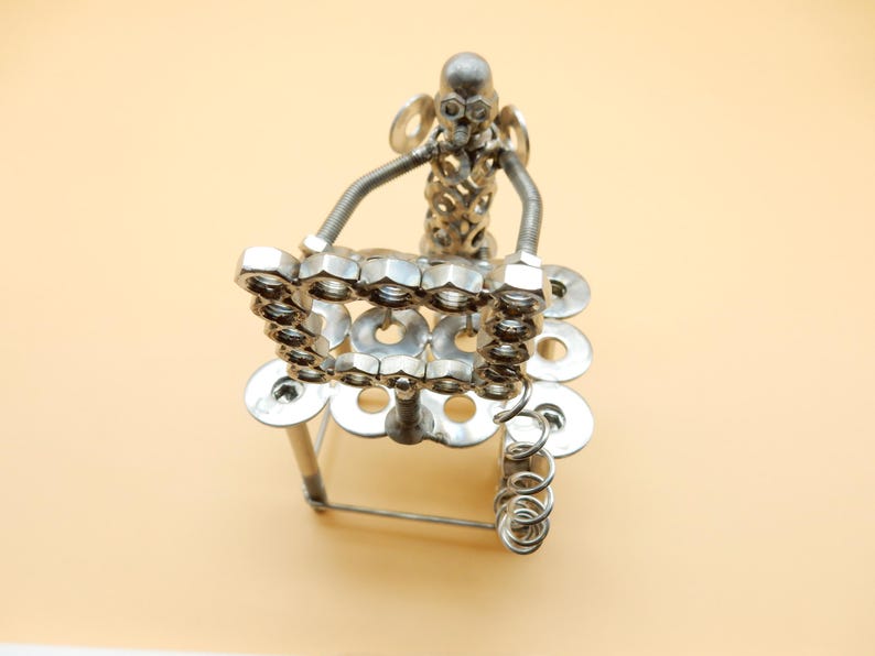 May include: A silver metal sculpture of a person sitting on a chair made of nuts and bolts. The sculpture is attached to a spring.