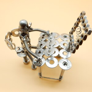 May include: A silver metal sculpture of a person sitting on a chair made of nuts and bolts.