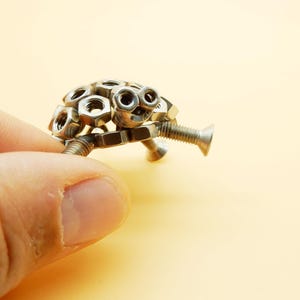 May include: A small, silver turtle sculpture made from nuts and bolts.