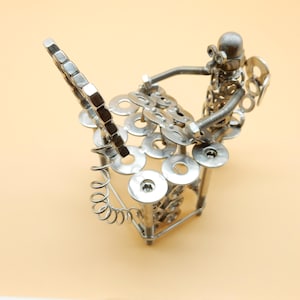 May include: A silver metal sculpture of a person playing a drum set made of nuts, bolts, and washers.