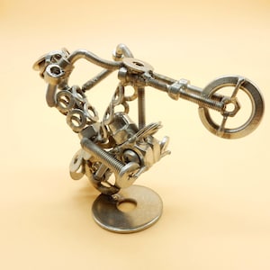 Könnte beinhalten: Eine silberne Metall-Motorrad-Skulptur aus Muttern, Schrauben und Unterlegscheiben. Das Motorrad steht auf seinem Hinterrad und ist in der Luft positioniert.