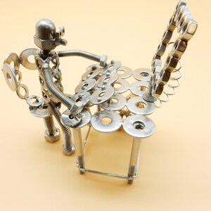 May include: A silver metal sculpture of a person playing a drum set made of nuts and bolts.
