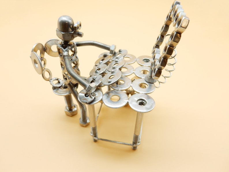 May include: A silver metal sculpture of a person playing a drum set made of nuts and bolts.