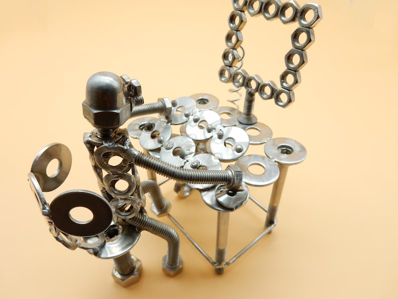 May include: A silver metal sculpture of a person playing a drum set made of nuts, bolts, and washers. The sculpture is sitting on a table made of the same materials.