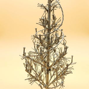 May include: A silver metal Christmas tree sculpture made from nuts, bolts, and wire. The tree is decorated with small metal rings and has a round base.