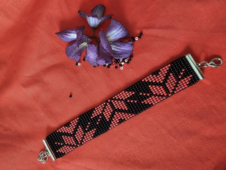 May include: A red and black beaded bracelet with a silver clasp. The bracelet features a geometric pattern of red and black beads.