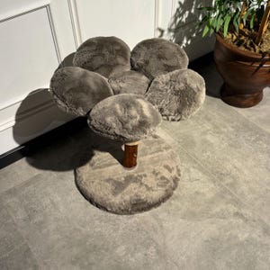 May include: A gray cat tree shaped like a flower with five soft, plush petals. The tree has a brown wooden post and a round, gray base.