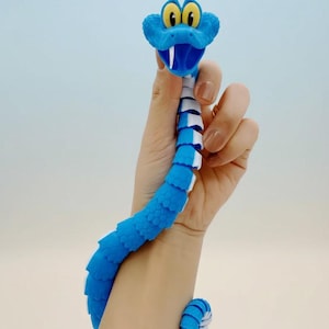 May include: A blue and white articulated snake toy with yellow eyes and a white fang. The toy is held in a hand and wrapped around a wrist. The snake's body is segmented, allowing for flexible movement.