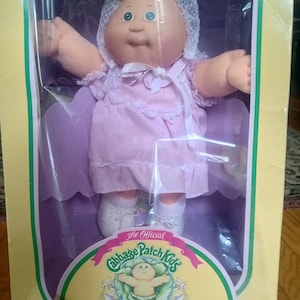 May include: A vintage Cabbage Patch Kids Preemie doll in its original box. The doll wears a pink dress and a white lace bonnet. The box features the Cabbage Patch Kids logo and the text "Preemie!" and "I'm unique. I'm adoptable!"