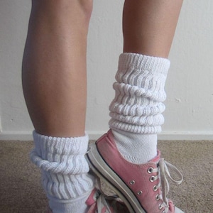 Può includere: Scarpe da ginnastica rosa in tela con lacci e suole bianche sono abbinate a calzini bianchi larghi. Le scarpe da ginnastica sono basse e classiche. I calzini sono spessi e a coste, creando un look casual e retrò.