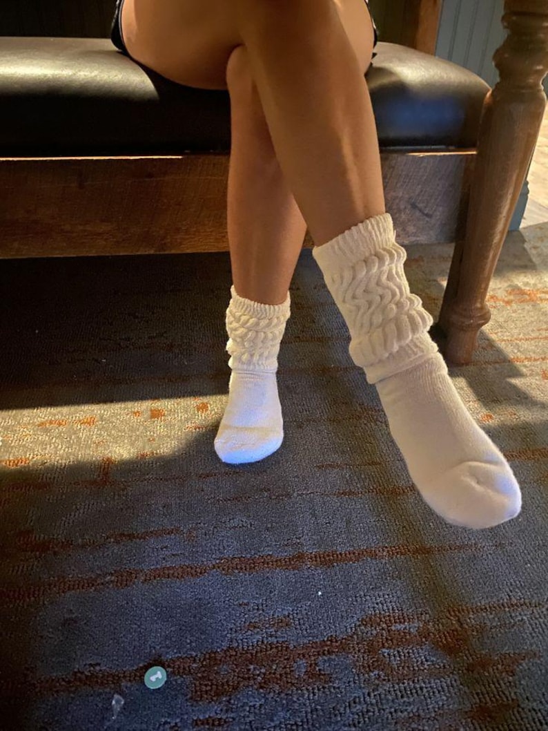 May include: A pair of white, slouchy socks with a ribbed texture. The socks are worn on the feet and ankles. The socks are made of a soft material and have a comfortable fit. The socks are a light cream color.