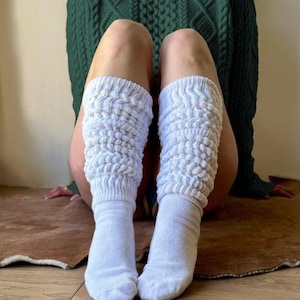 May include: A pair of white, textured slouch socks. The socks are worn with a dark green cable-knit sweater. The socks are made of a soft material and are designed to be worn casually. The socks are a light, neutral color.
