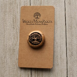 May include: A wooden button with a tree of life design. The button is brown and has a natural wood finish. The text "Wooly Moss Roots Handmade Artisan Buttons" is printed on a brown card behind the button.