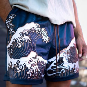 May include: Navy blue shorts featuring a white and brown wave design. The shorts have a drawstring and pockets. The wave pattern is embroidered, adding texture and detail to the garment. A stylish and comfortable choice for casual wear.