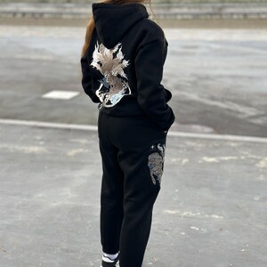 May include: Black hoodie and sweatpants set with embroidered dragon and tiger designs. The hoodie features a large dragon design on the back, while the sweatpants have a tiger design on the leg. The set is worn with white sneakers.