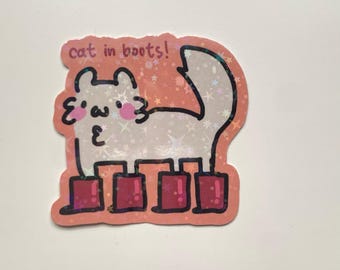 Puede incluir: Una pegatina rosa y blanca con un gato de dibujos animados que lleva botas rojas. El gato es blanco con mejillas rosas y una nariz rosa. El texto "cat in boots!" está escrito encima del gato.
