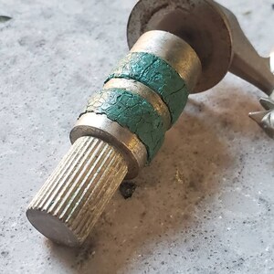 Puede incluir: Una v&aacute;lvula de metal plateado con dos anillos de goma verde. La v&aacute;lvula tiene un extremo roscado y una parte superior plana.