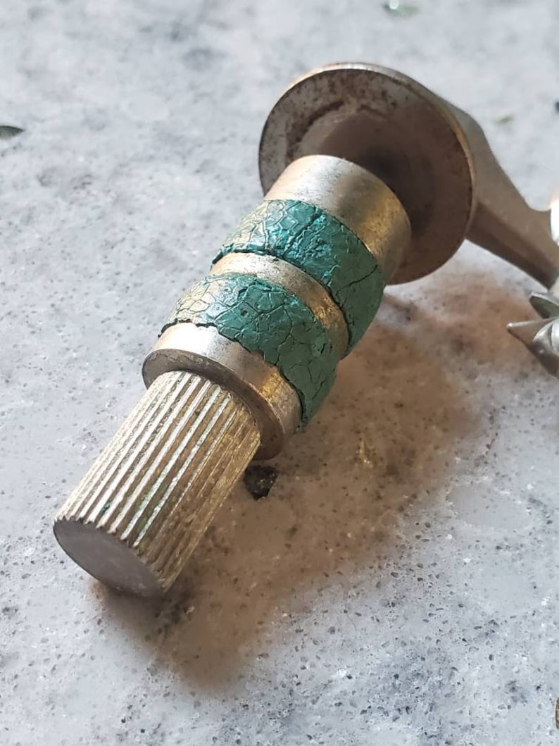 Puede incluir: Una v&aacute;lvula de metal plateado con dos anillos de goma verde. La v&aacute;lvula tiene un extremo roscado y una parte superior plana.