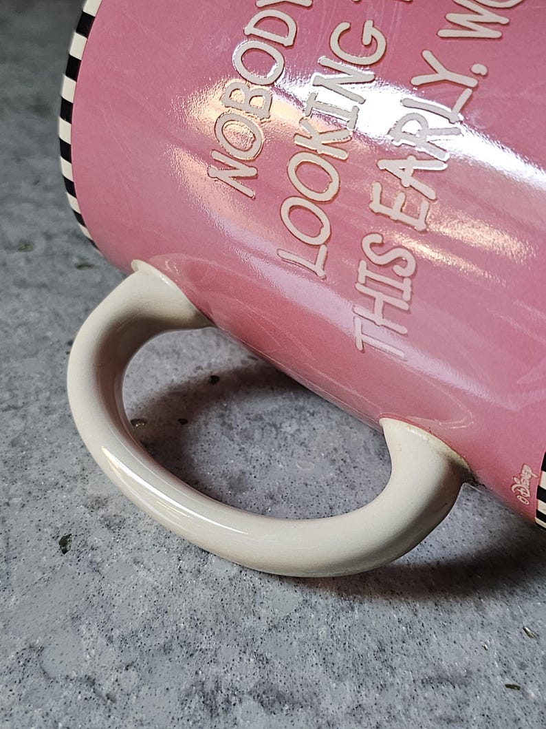 May include: Pink ceramic mug with the text "NOBODY LOOKING THIS EARLY". The mug has a white handle and a black and white striped rim. The Disney logo is visible on the side.
