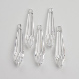 May include: Five clear crystal teardrop-shaped pendants. The pendants are faceted and have a pointed tip.