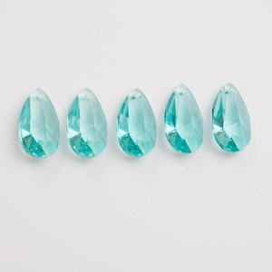 May include: Five aqua-colored, faceted teardrop-shaped crystal beads. Each bead has a small hole at the top for stringing. The crystals are arranged in a row against a white background.