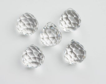 May include: Five clear crystal prisms, each with a faceted design, are arranged on a white surface.
